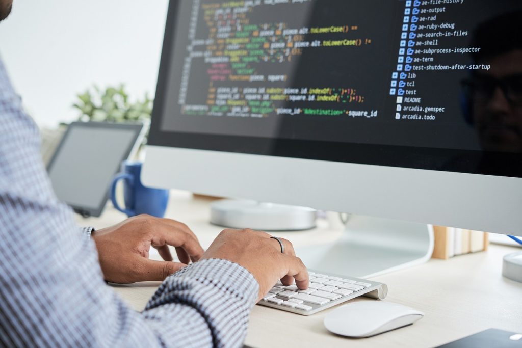 Person typing code on large desktop monitor